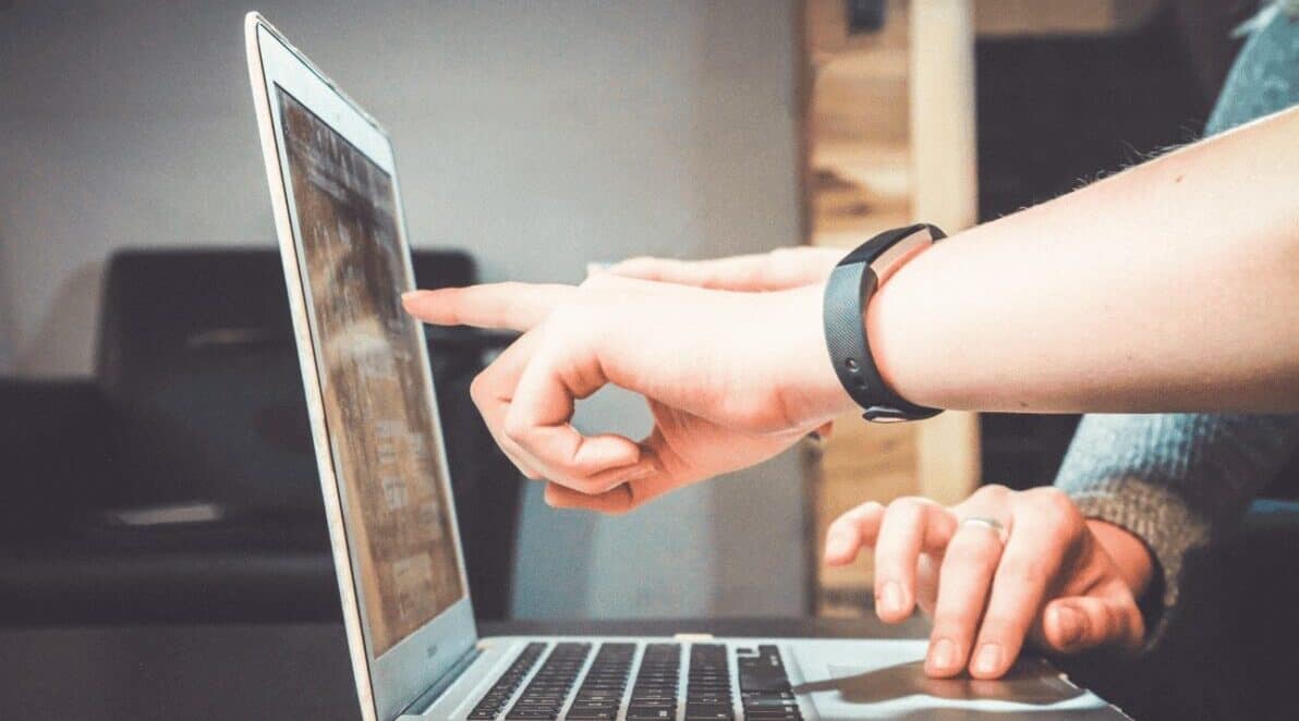 Two people are interacting with a laptop. One persons hand is pointing at the screen, while the other rests on the keyboard. They appear to be collaborating or discussing something displayed on the laptop.